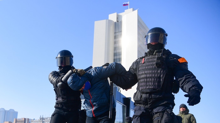Deux policiers encadrent un manifestant. L'un le tient par le bras, l'autre lui tient la tête penchée.