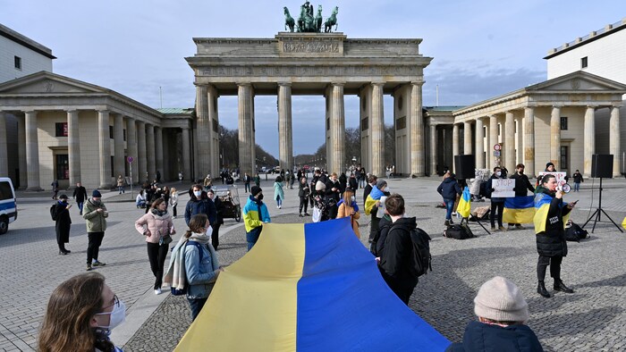 Des manifestants tiennent un immense drapeau de l'Ukraine sur une place de Berlin.