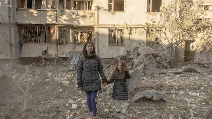 Une femme et sa fille marchent dans les décombres.
