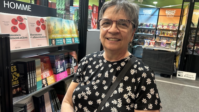 Une femme souriante se tient devant un kiosque de livre.