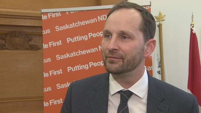 Le chef du Nouveau Parti démocratique, Ryan Meili, porte un costume et parle aux médias lors d'une conférence de presse.