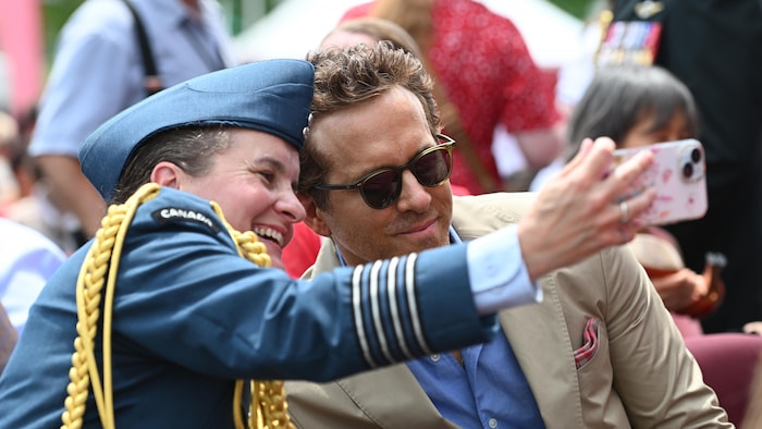 Ryan Reynolds takes a selfie with a woman. canada day marked "canadian pride"