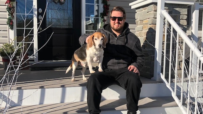Le jeune homme est assis sur des marches devant l'entrée d'une maison et caresse un chien.