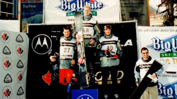 Quatre hommes tenant chacun une planche à neige. L'un d'eux est sur le côté, et trois autres sont placés sur un podium. Celui qui est le plus haut sur le podium est Ryan Wedding.