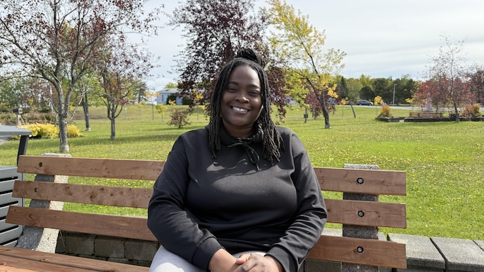 Souriante, Sabine Dasemé est assise sur un banc dans un parc.