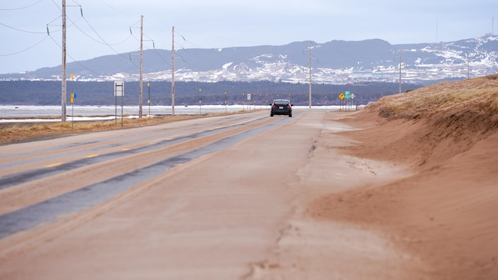 Du sable sur la route, avec des dunes à droite.