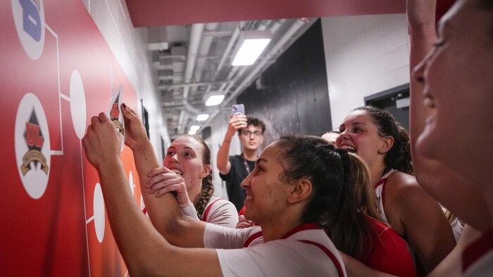 Les joueuses posent le logo du Rouge et Or sur un tableau géant du tournoi installé sur un mur. Le logo signifie que le Rouge et Or passe au tour suivant.  
