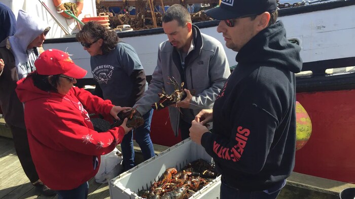 Michael Sack et d'autres membres de sa communauté examinent des homards sur un quai.