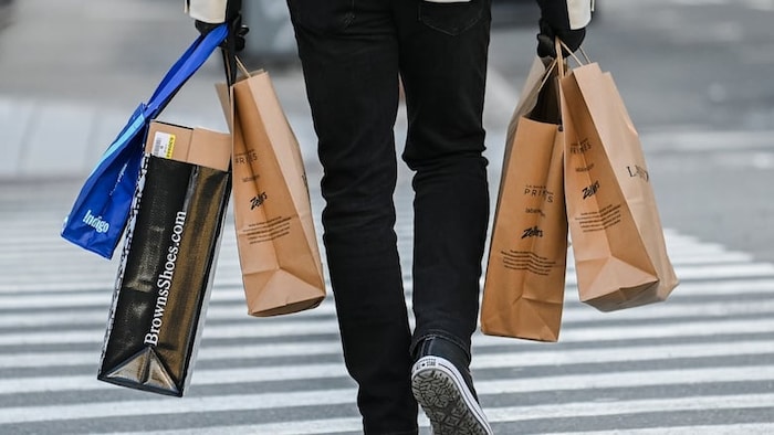 Une personne tient des sacs de magasinage dans ses deux mains en marchant dans une rue de Montréal en décembre 2024.