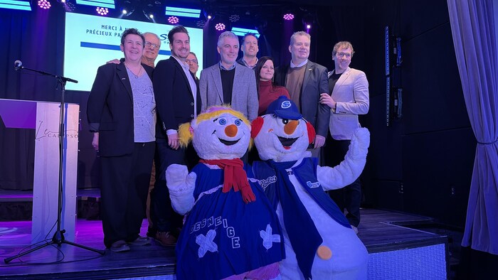 Plusieurs personnes posent avec une mascotte sur une scène.