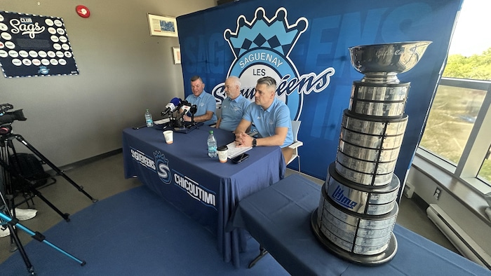 Trois personnes sont assises à une table à côté d'une autre table avec un trophée.