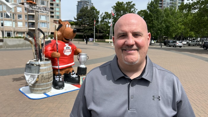 Dominic Ricard pose devant la statue d'une mascotte dans un parc.