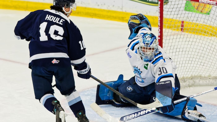 Un joueur de hockey sur glace qui lance une rondelle dans un but protégé par un gardien de l'autre équipe. 