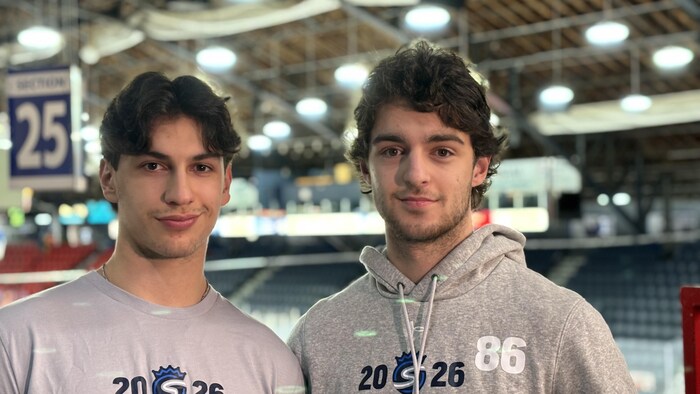 Deux joueurs de hockey habillés en civil dans un aréna.