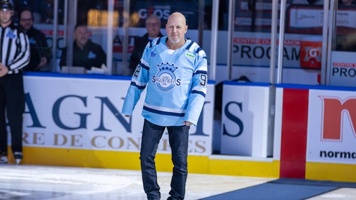 Un homme avec un chandail de hockey marche sur un tapis sur une patinoire.