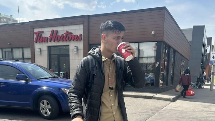 Sahil Kumar dans la rue avec une valise, qui boit un café.