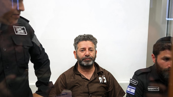 Un homme assis dans un box, entouré de deux policiers.