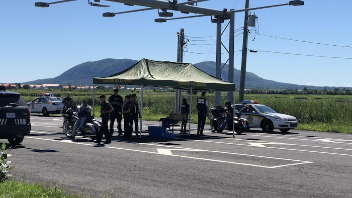 Des policiers de la Sûreté du Québec installés sous une tente placée sur la route.