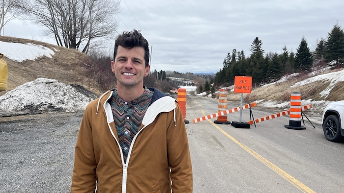 Un homme sourit à la caméra devant une route fermée.