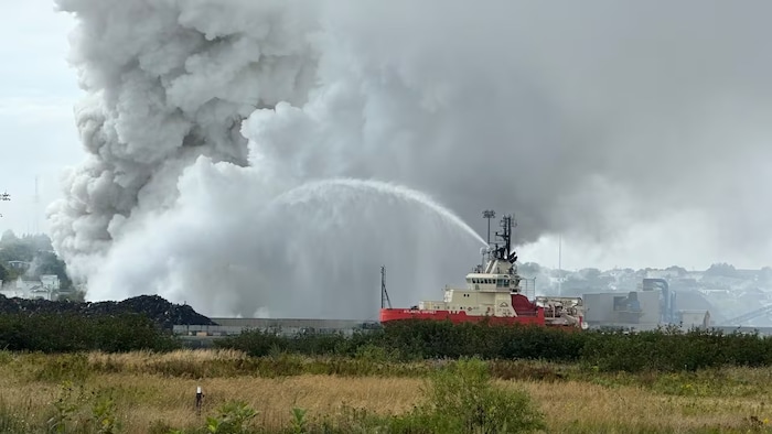 Un bateau équipé d'une lance d'incendie arrose le brasier.