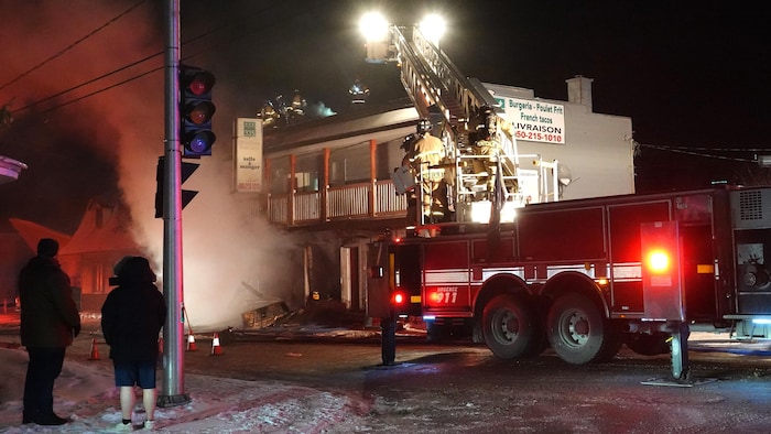 Les pompiers sont déployés devant un immeuble commercial en feu qui abrite aussi des logements, sous les yeux de badauds.