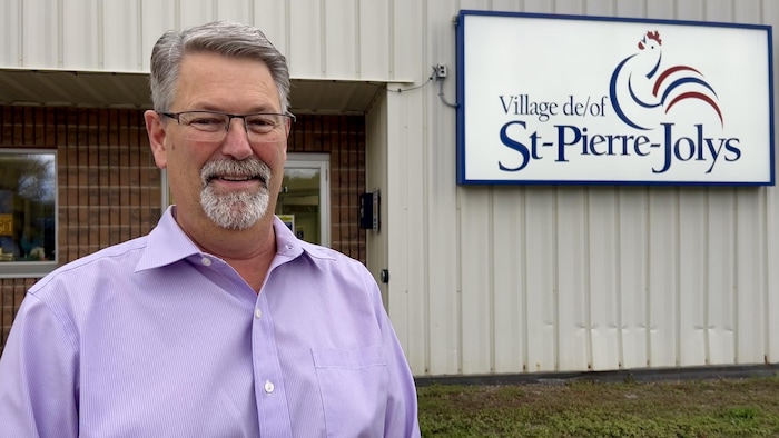 Raymond Maynard est debout dehors devant un panneau du village de Saint-Pierre-Jolys.