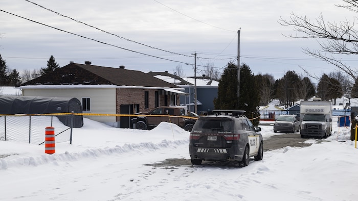 Des véhicules policiers sont stationnés devant une maison.