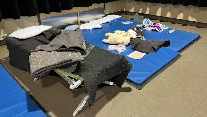 Un lit de camp avec des couvertures à côté de matelas étendus par terre.