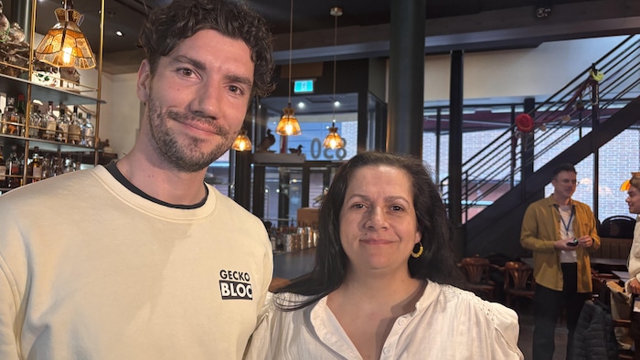 Deux personne regardent la caméra debout dans un restaurant.