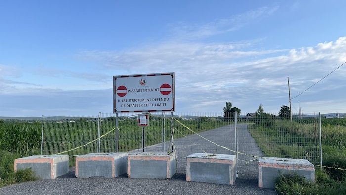 Une affiche "passage interdit", une clôture et des blocs de bétons empêchent de circuler sur une route de campagne.