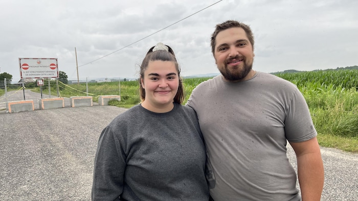 Près de blocs de béton bloquant l'accès à une route et une affiche indiquant l'interdiction de circuler, Cindy Nolet et Pierre-Luc Trottier posent en se tenant tout près, avec un sourire.