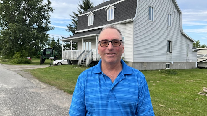 Sylvain Trottier pose pour la caméra, devant une maison.