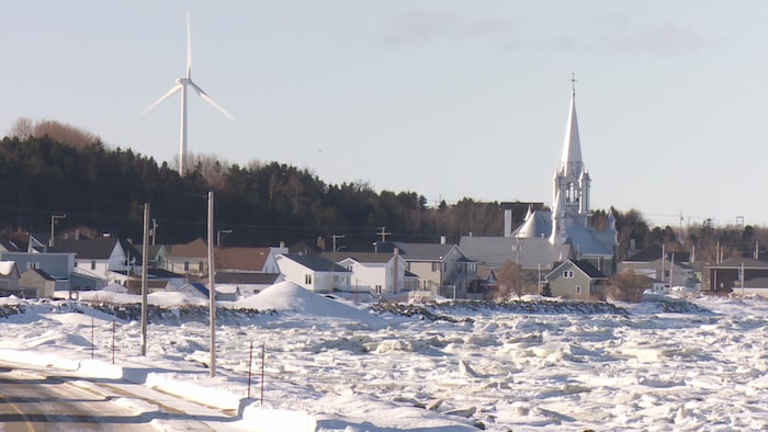 Village sous la neige avec l'église et une éolienne.