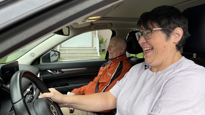 Sylvie Bédard au volant de sa voiture en compagnie de M. Talbot assis sur le siège passager.