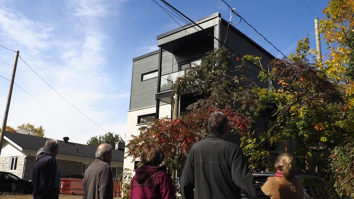 Cinq résidents regardent, de dos, l'immeuble à logements de trois étages apparu sur la rue Richer.