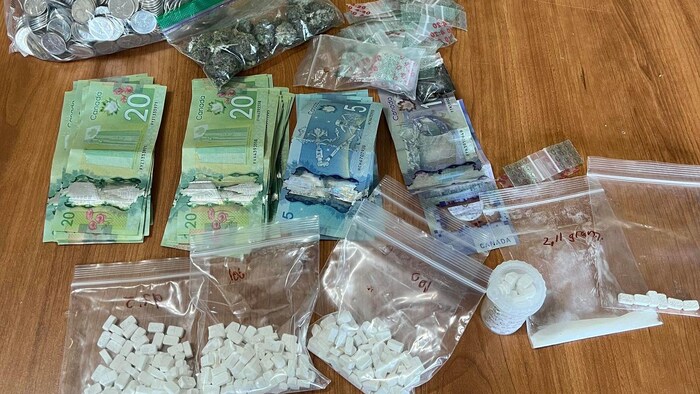 Des comprimés, du cannabis et des billets de banque sont déposés sur une table.