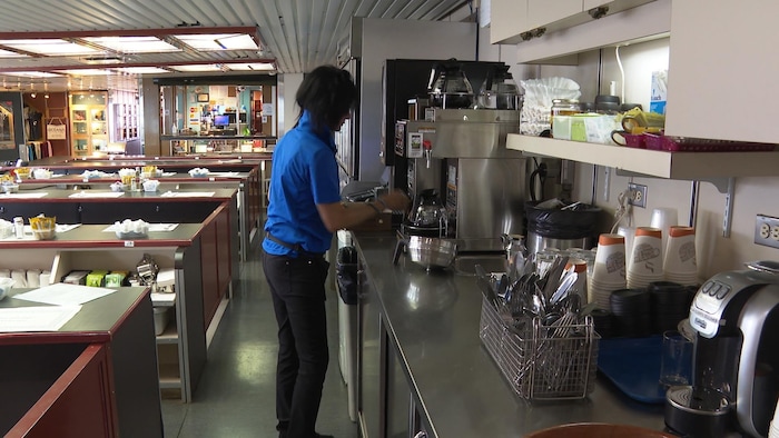 Une femme devant une machine à café dans une salle de restaurant.