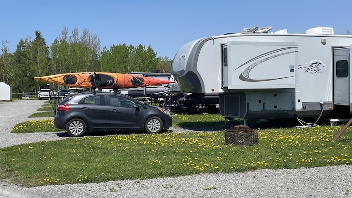 Une voiture avec un kayak sur le toit à côté d'une roulotte.