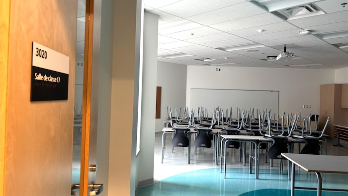 La lumière naturelle du jour éclaire une salle de classe avant l'arrivée des élèves. Les chaises sont posées à l'envers sur les pupitres.