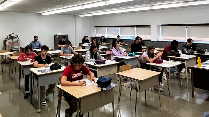 Des adolescents sont assis à leur pupitre dans une salle de classe. 