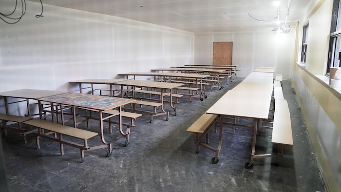 Des tables de cafétéria sont alignées dans un local restreint. 