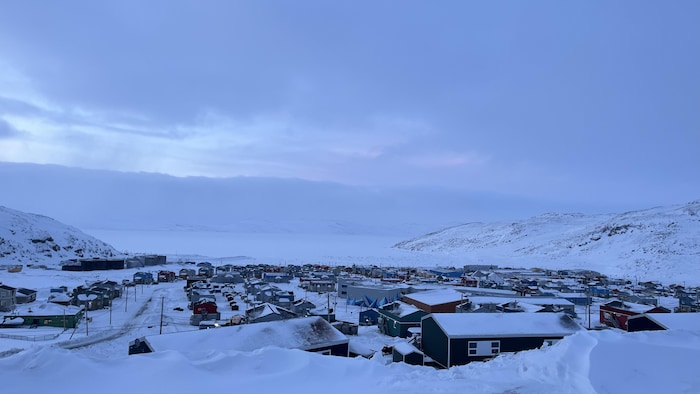 Des maisons sont entourées de montagnes et d'une baie gelée.