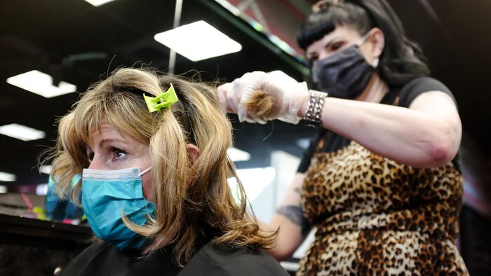 Une coiffeuse est debout derrière une cliente assise. Les deux portent un masque sur leur visage.