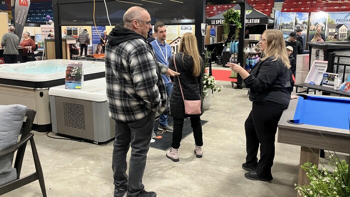 Des gens du public et des exposants échangent près d'une table de billard et d'un spa.