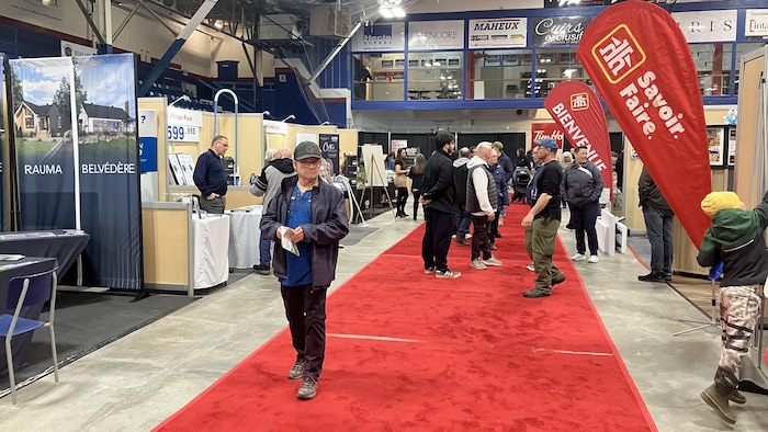 Des gens échangent avec des exposants et un homme marche dans l'allée.