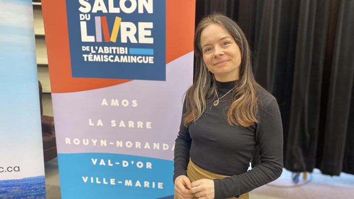Carine Paquin devant une affiche du Salon du livre de l'Abitibi-Témiscamingue.  