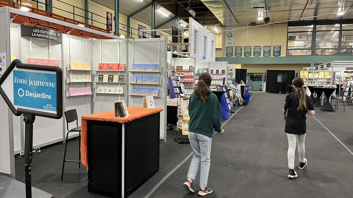 Deux personnes marchent entre les kiosques du 48e Salon du livre de l'Abitibi-Témiscamingue à La Sarre.