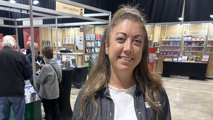 Une femme pose pour une photo. Il y a des kiosques et des &eacute;talages de livres derri&egrave;re elle.