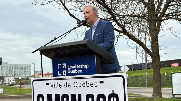 Sam Hamad prend la parole à l’extérieur. Il se tient debout derrière un pupitre aux couleurs du parti Leadership Québec.