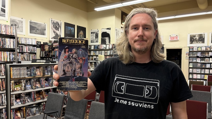 Sam Meech pose au Cinoche Club Vidéo avec la cassette VHS du film Beetlejuice.